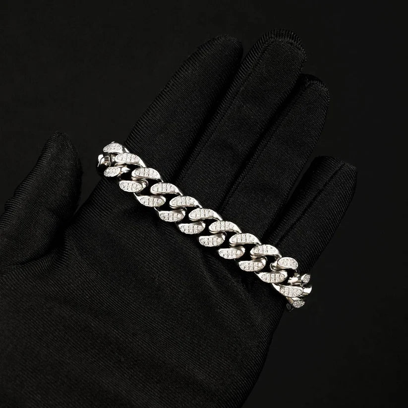 A silver Cuban link chain bracelet paved with, displayed on a black textured glove