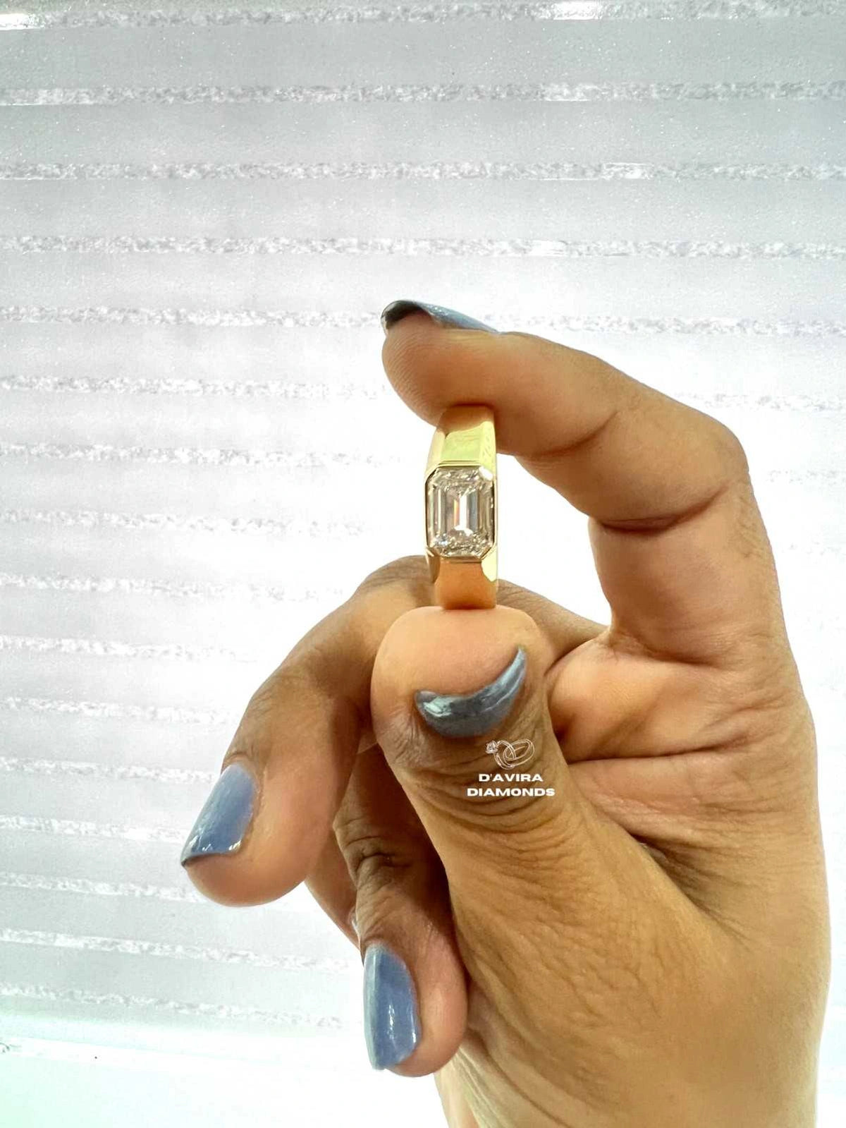 Bezel set emerald cut lab diamond yellow gold ring held between fingers