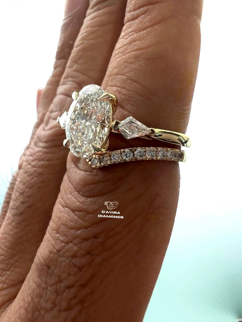 side view of a hand wearing a gold ring set with a oval-cut diamond and a smaller diamond band