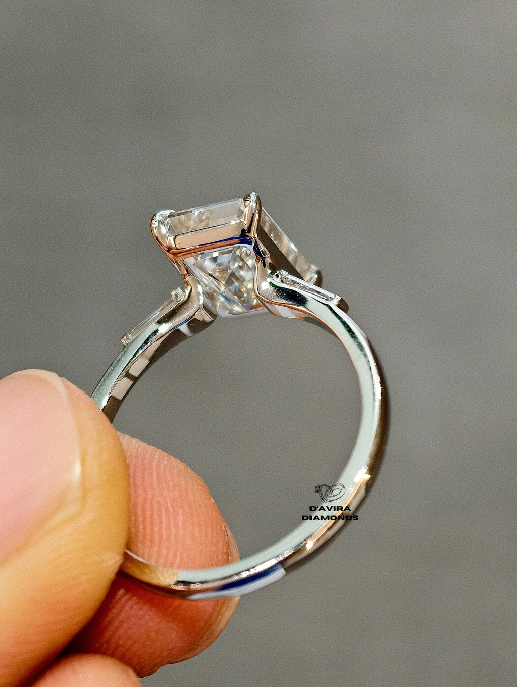 back view of an emerald-cut diamond engagement ring held hand