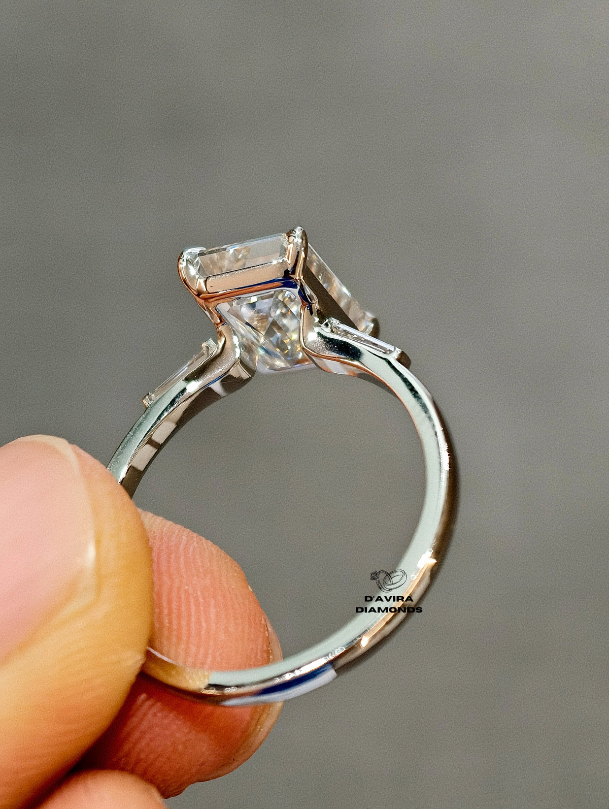 back view of an emerald-cut diamond engagement ring held hand