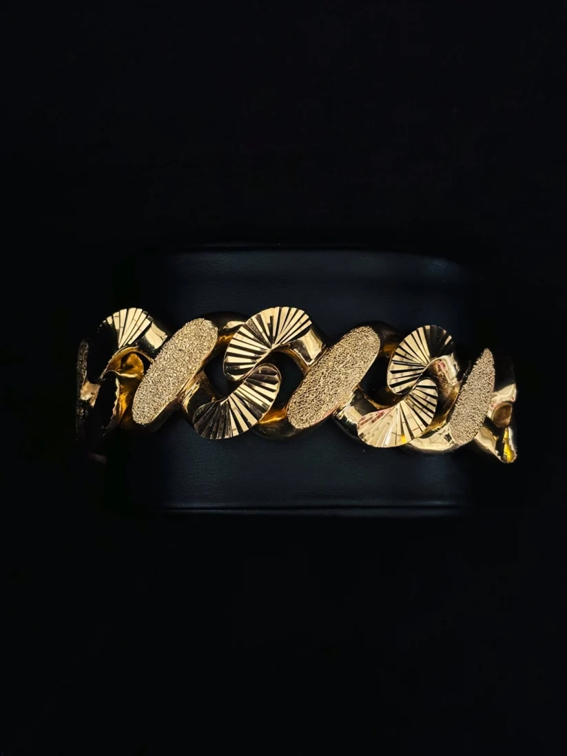 A wide chain bracelet with textured oval and fan-shaped links, displayed on a black background