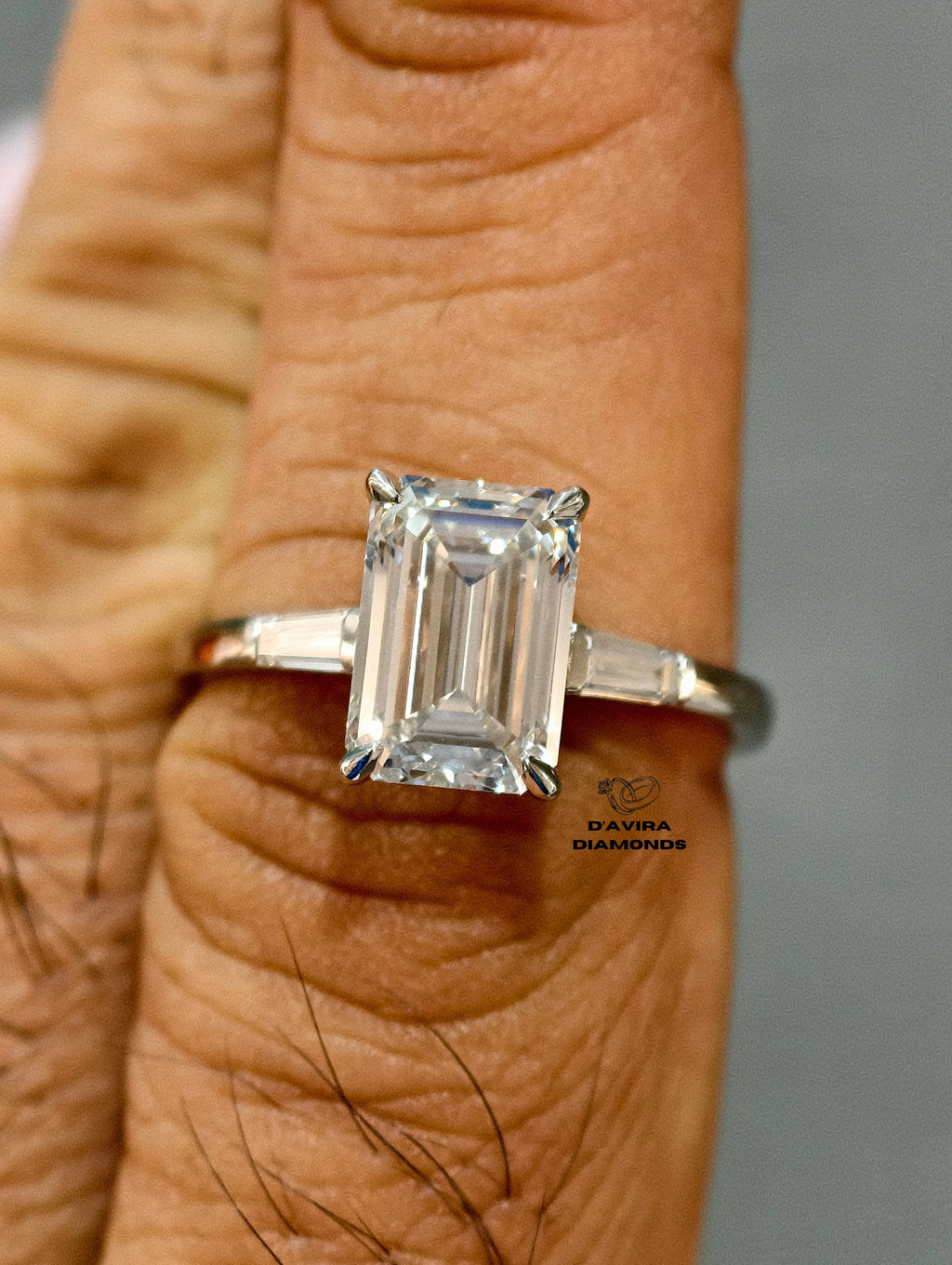 An emerald-cut diamond ring on a white band worn on a person finger