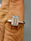 An emerald-cut diamond ring on a white band worn on a person finger