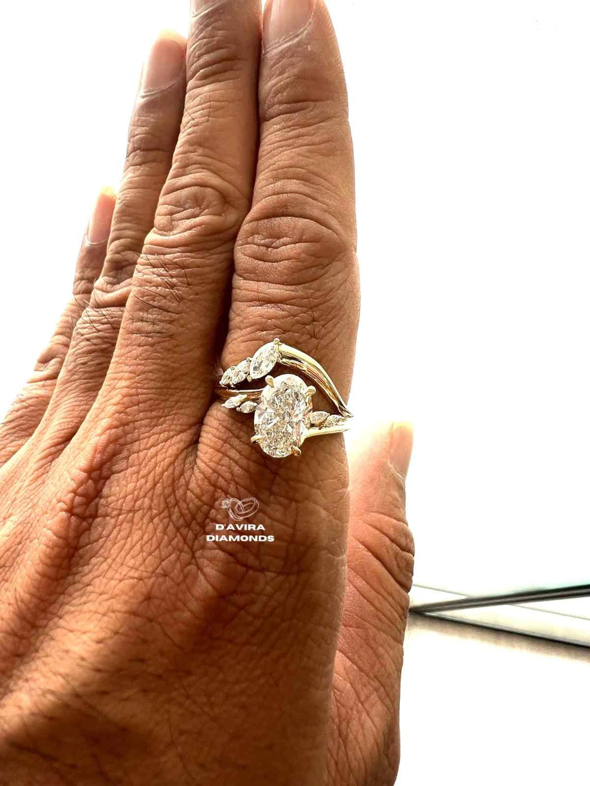 A close-up of a hand wearing a gold ring with oval center stone and smaller side stones