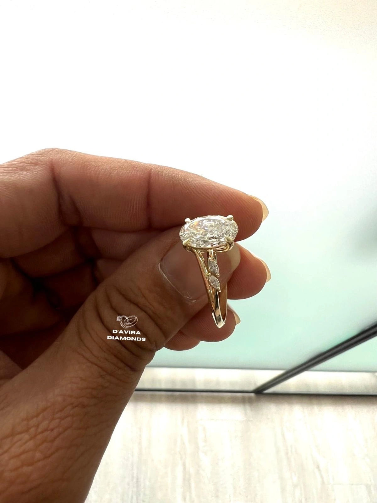 A hand holding a yellow gold engagement ring with a oval cut diamond
