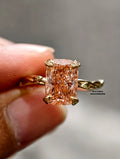 A close-up of a hand holding a yellow gold ring with a cushion-cut peach diamond