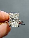 A close-up of a radiant-cut diamond ring held between fingers