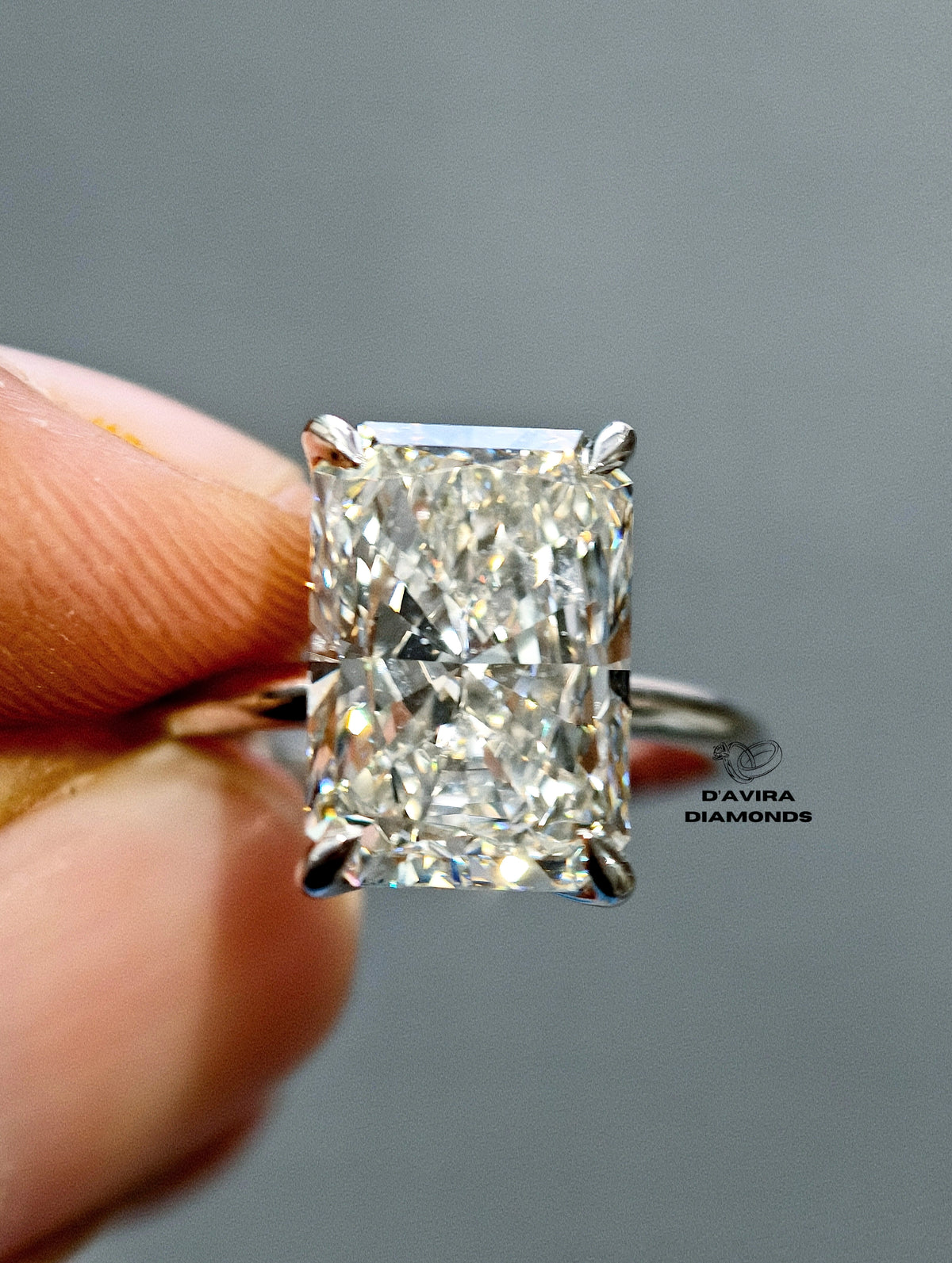A close-up of a radiant-cut diamond ring held between fingers