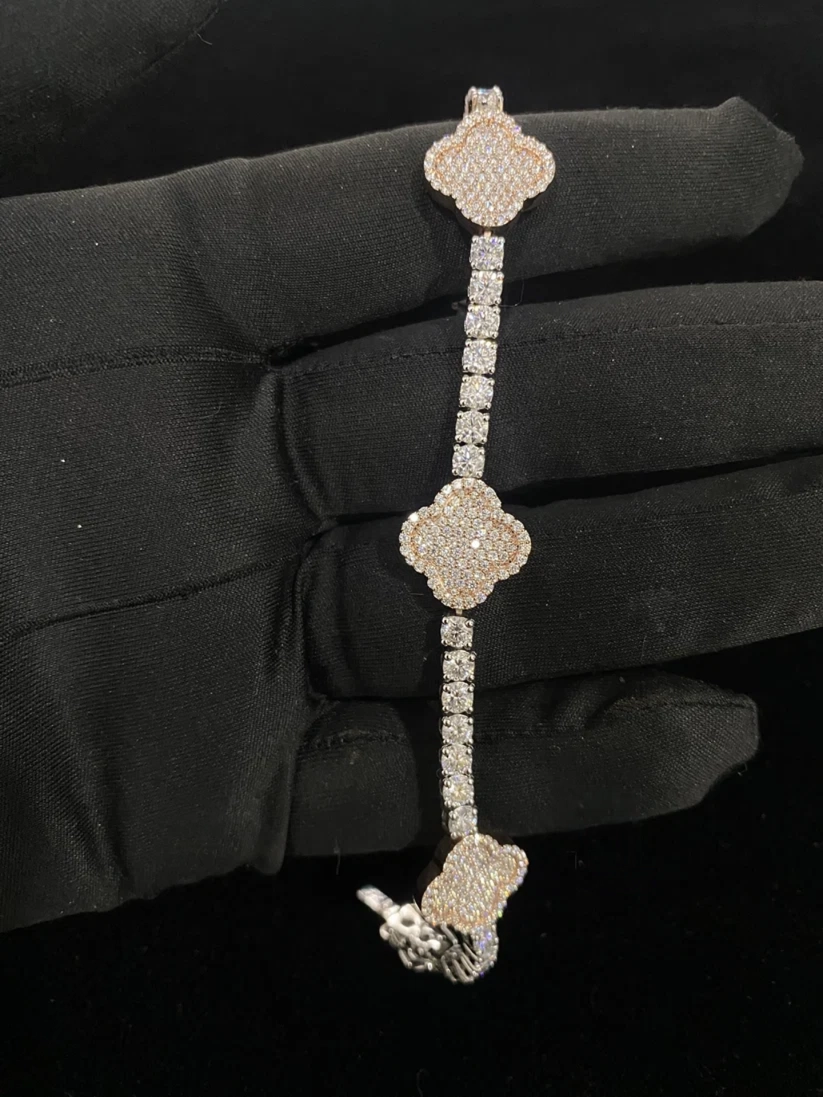 A three-piece diamond bracelet with clover-shaped motifs and a pave band, held by a hand wearing a black glove