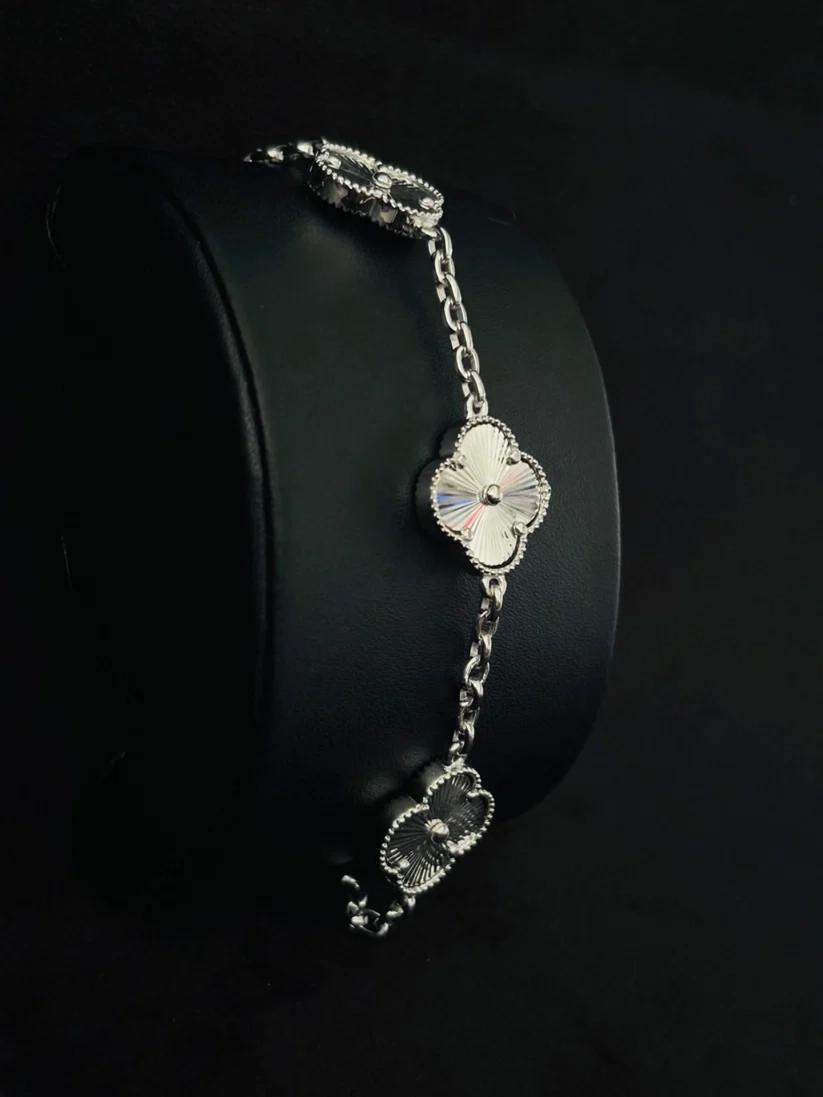 A silver chain bracelet with three clover-shaped links, each featuring a white enamel center on stand