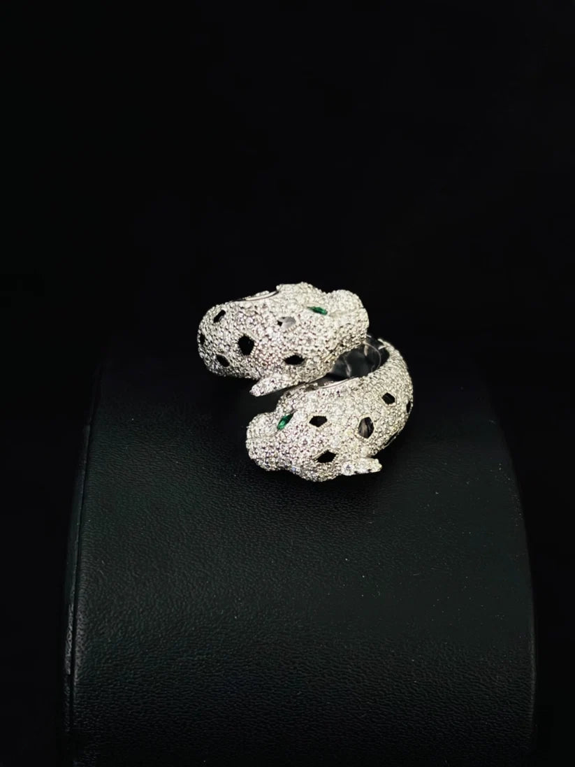 A silver ring designed as a coiled snake, heavily embellished with pave stones and accented with two small green gemstones