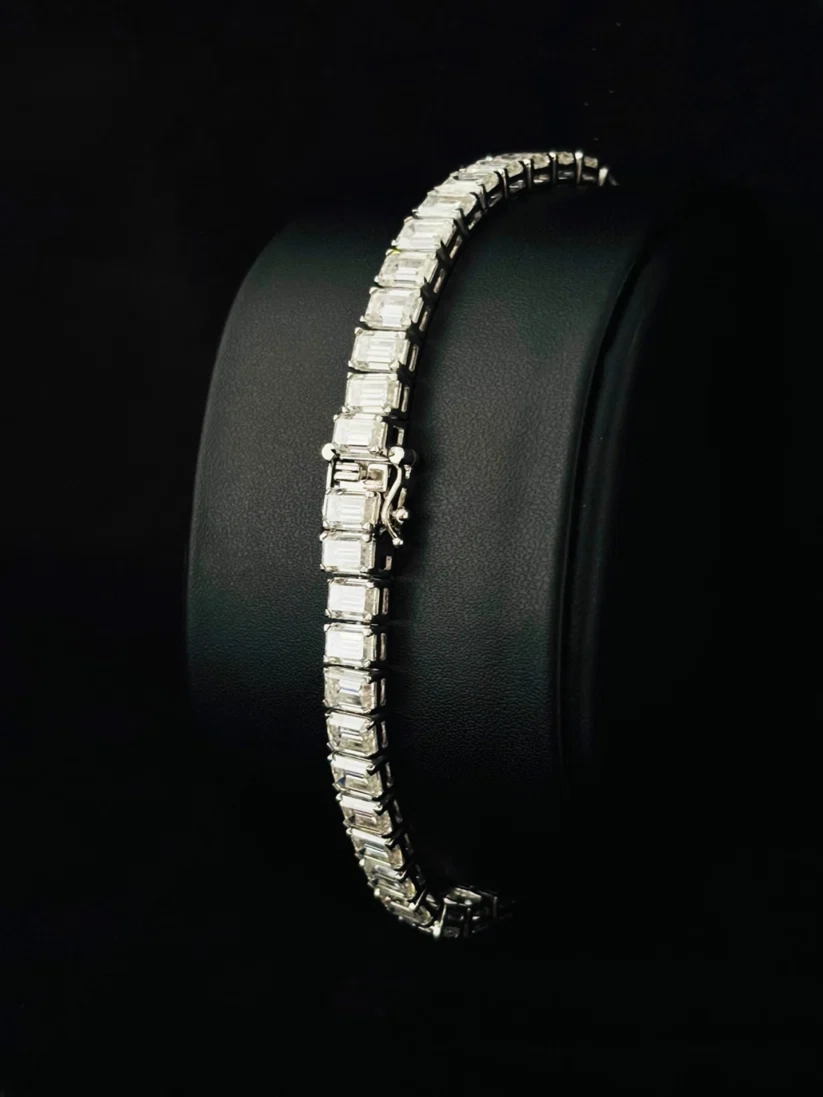 Emerald cut diamond tennis bracelet in a silver setting displayed on a black jewelry stand