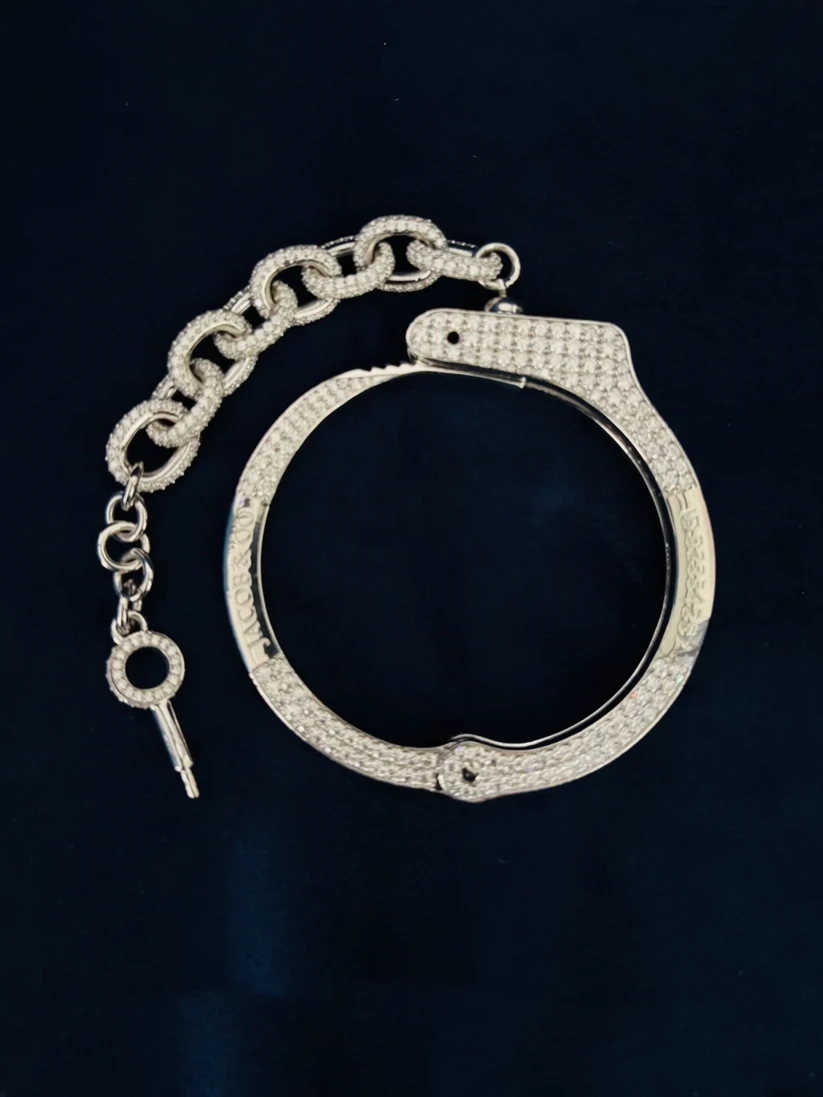 Silver handcuffs encrusted with diamond, chain link extension and key, displayed on a dark navy background