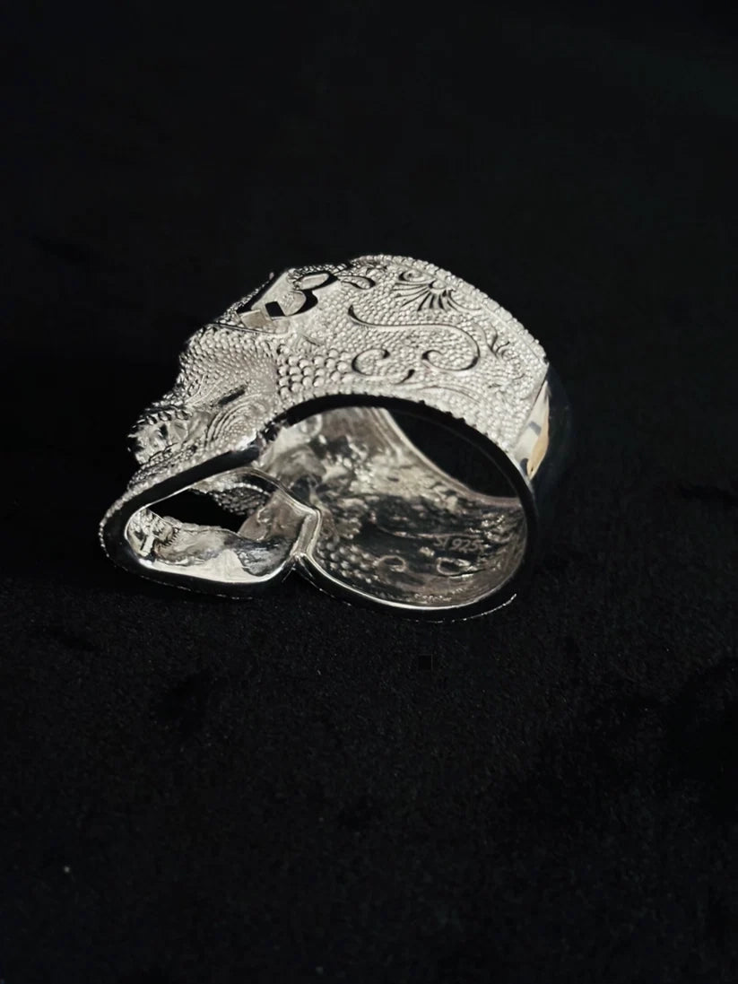Side profile view of a highly detailed, engraved silver skull ring against a black background