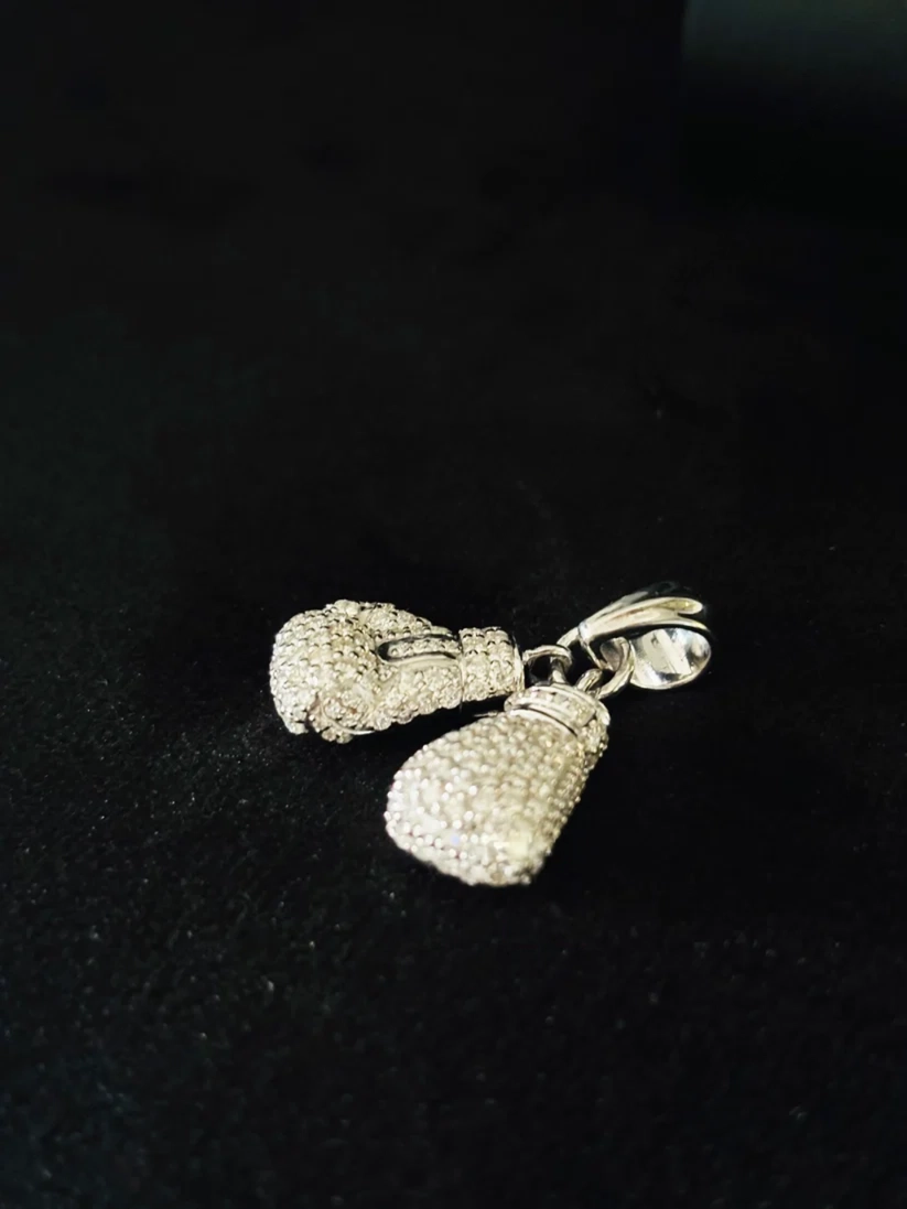 Iced-out silver boxing gloves pendant necklace charm against a black background