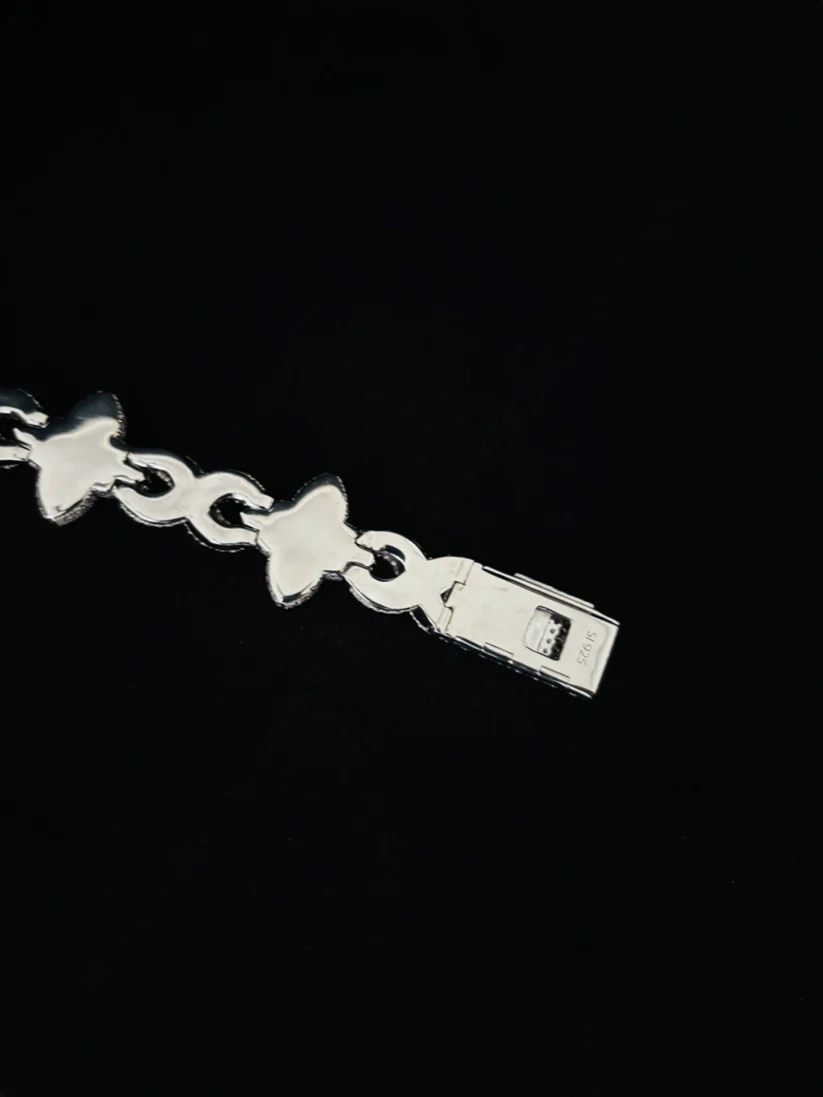 A close-up of a silver chain bracelet featuring butterfly-shaped links and a rectangular tag