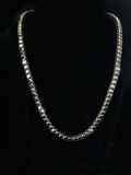 Single-row diamond tennis chain necklace displayed on a black bust mannequin