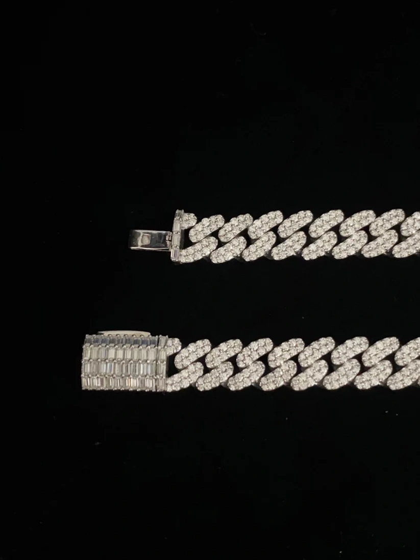 Diamond-encrusted silver Cuban link chain with a custom baguette diamond clasp on a black background