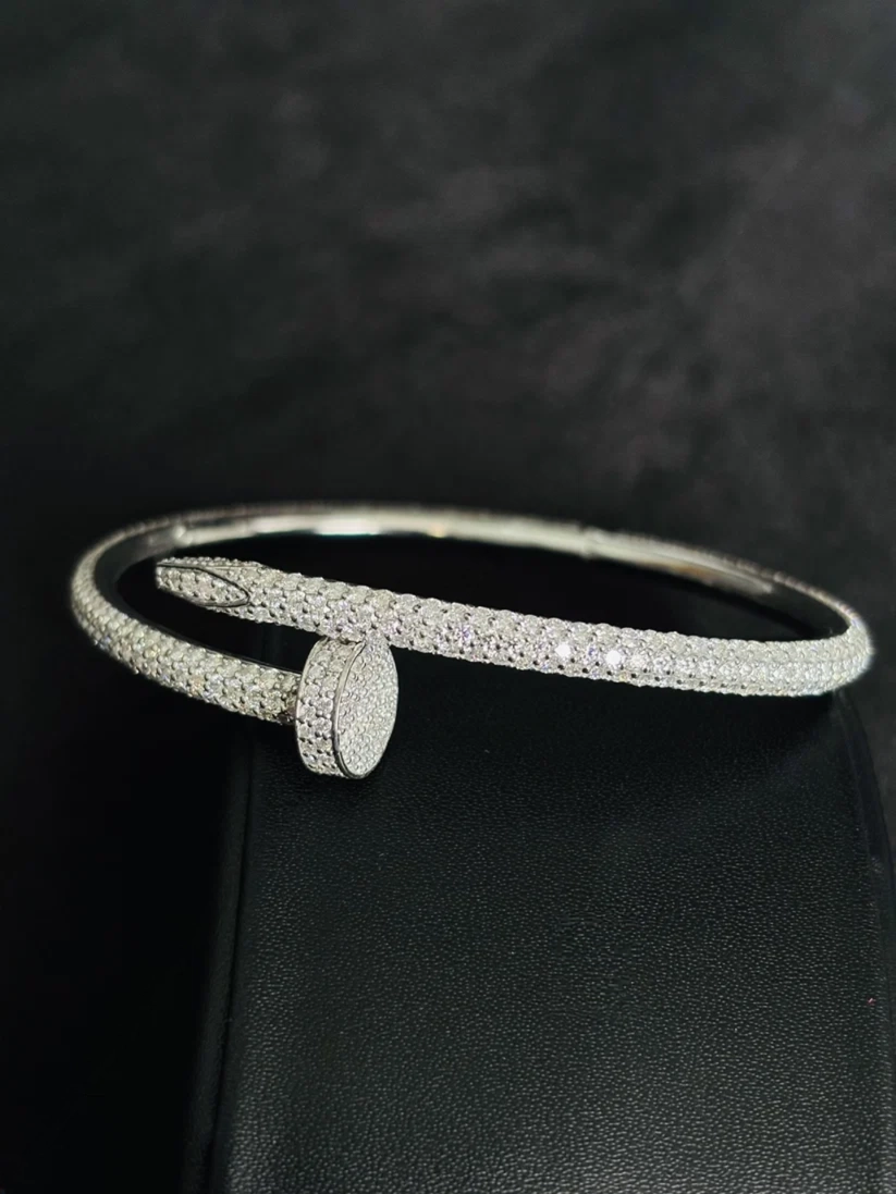 A silver snake-bone bangle bracelet paved with diamond, displayed on a black textured surface