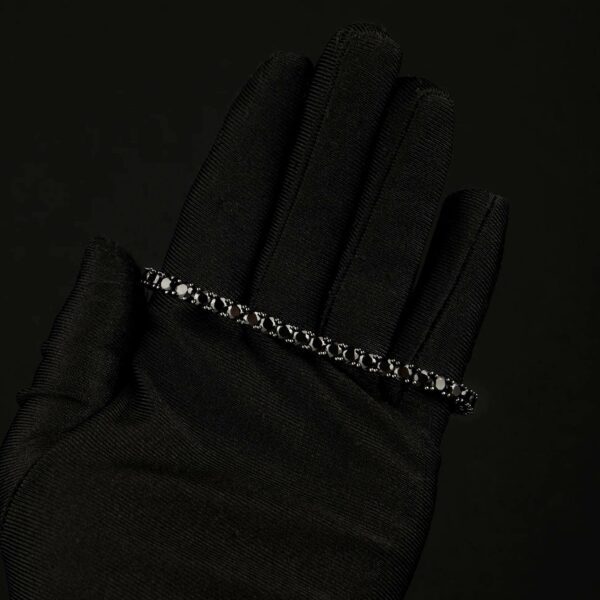 A black satin glove worn on a hand, featuring a delicate silver beaded bracelet with diamond draped across the back of the hand