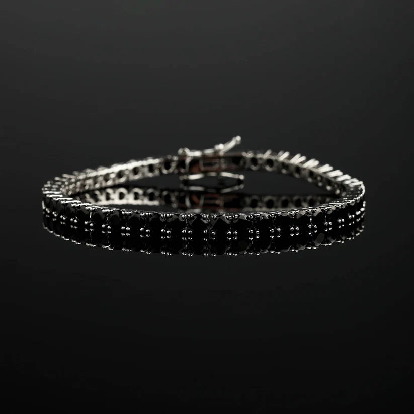 A silver tennis bracelet with black stones, shown on a reflective black surface against a dark background