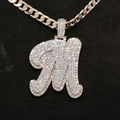 front view Iced out cursive letter M pendant necklace with diamonds on a silver Cuban link chain.