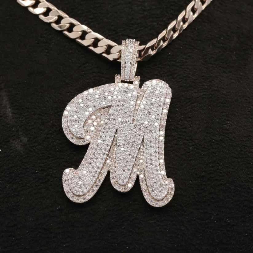 front view Iced out cursive letter M pendant necklace with diamonds on a silver Cuban link chain.