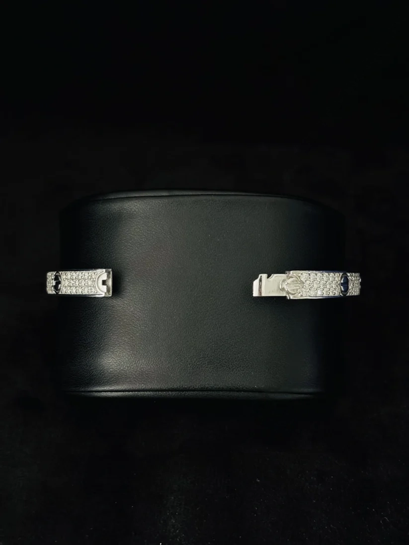 A silver diamond-encrusted cuff bracelet displayed on a black cylindrical stand against a dark background