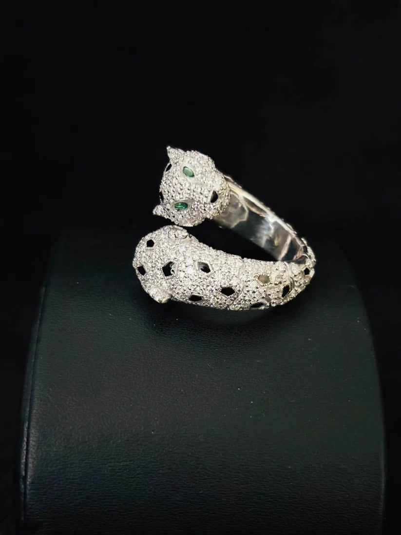 A silver cat-shaped ring with small green gemstone eyes and black dotted details on stand 