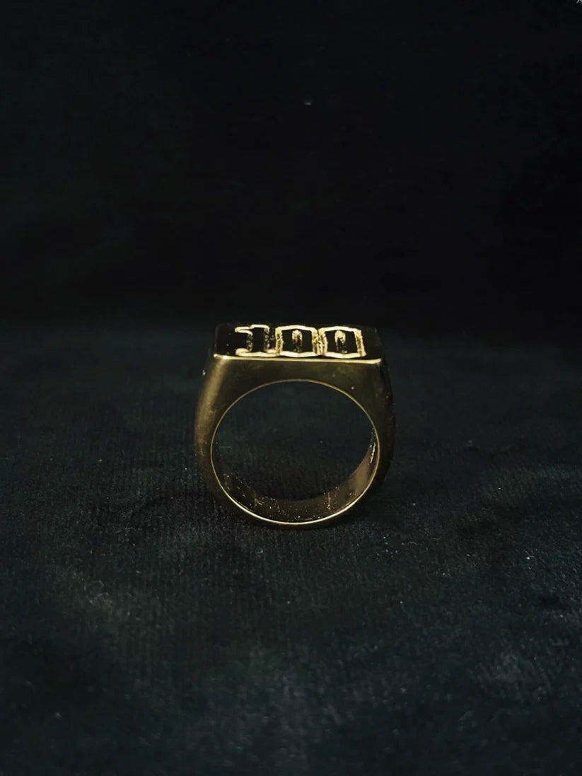 Close up view of a metallic gold plated typography signet ring