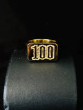 A Front view gold plated signet ring with the number '100' engraved on a black textured display stand