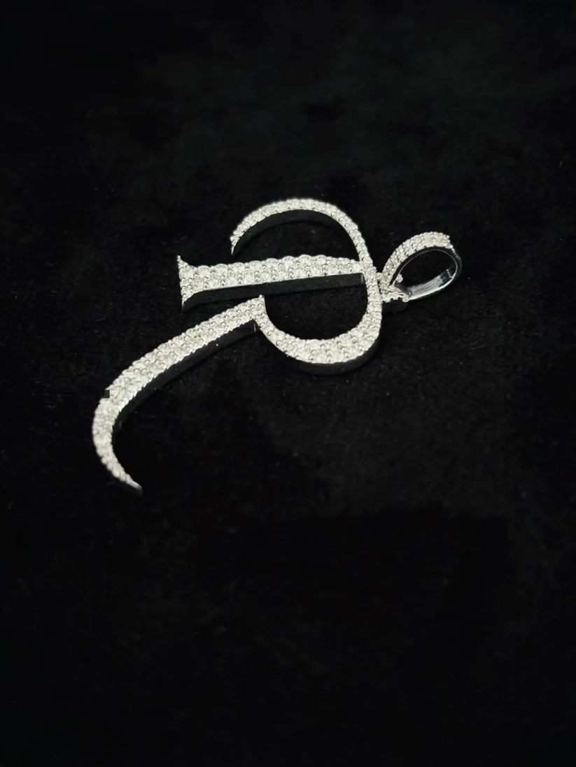 Silver cursive letter R initial pendant necklace paved with diamonds on a black background.