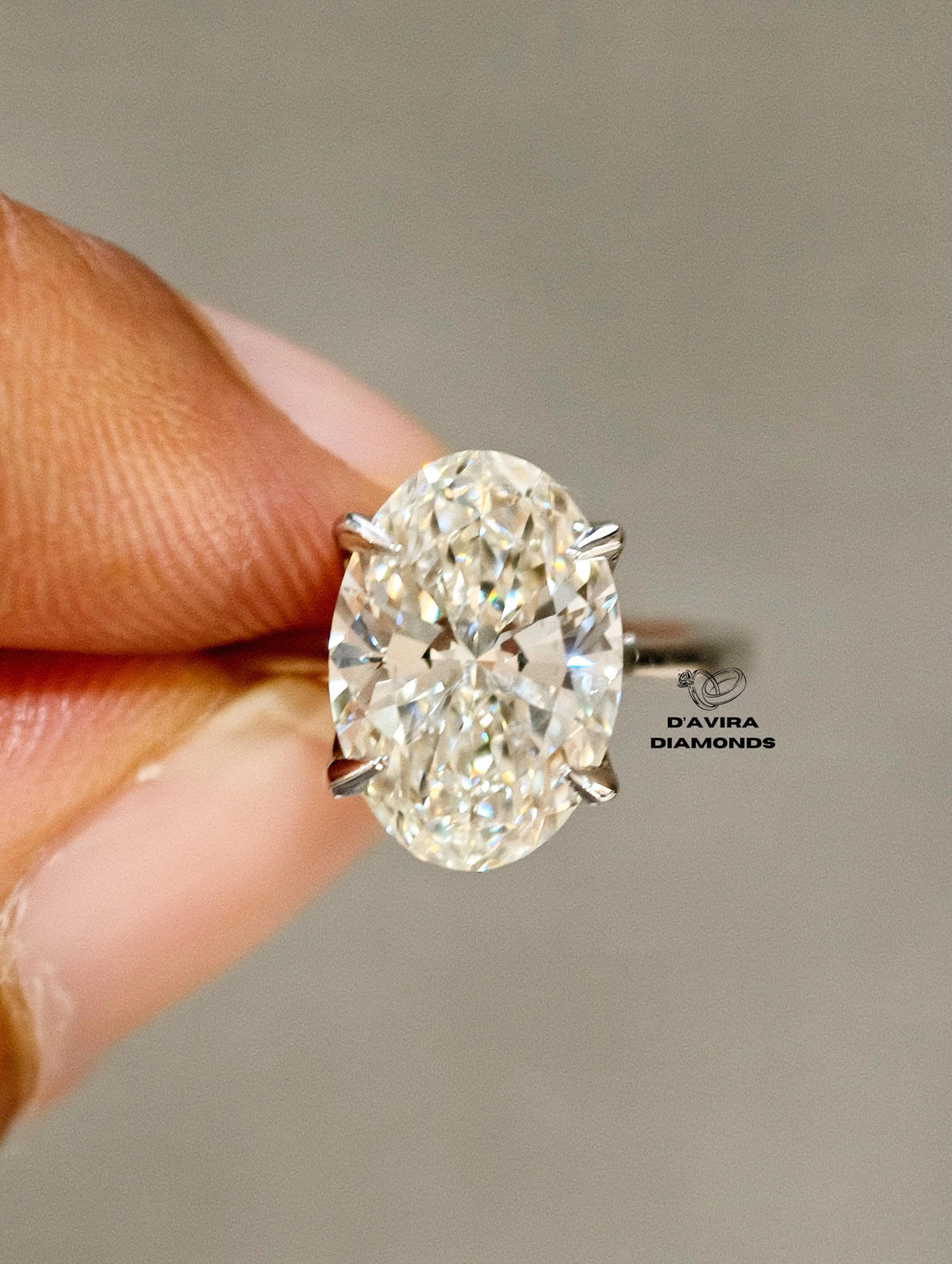 A close-up of a hand holding a brilliant oval-cut diamond ring 