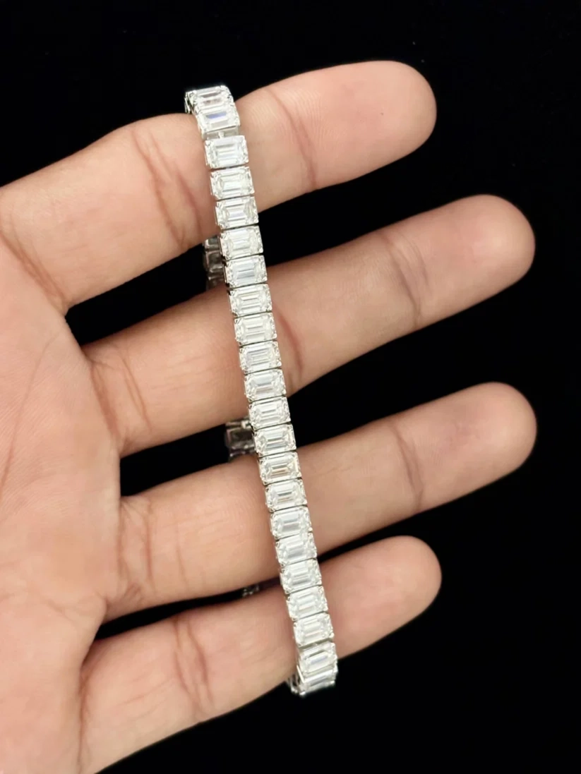 A hand holding an elegant silver tennis bracelet with step-cut emerald diamonds