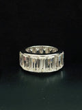 A wide silver ring featuring a row of baguette-cut diamond, photographed against a solid black background