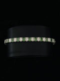 Tennis bracelet features alternating emerald-cut green, and baguette-cut diamond in a silver setting