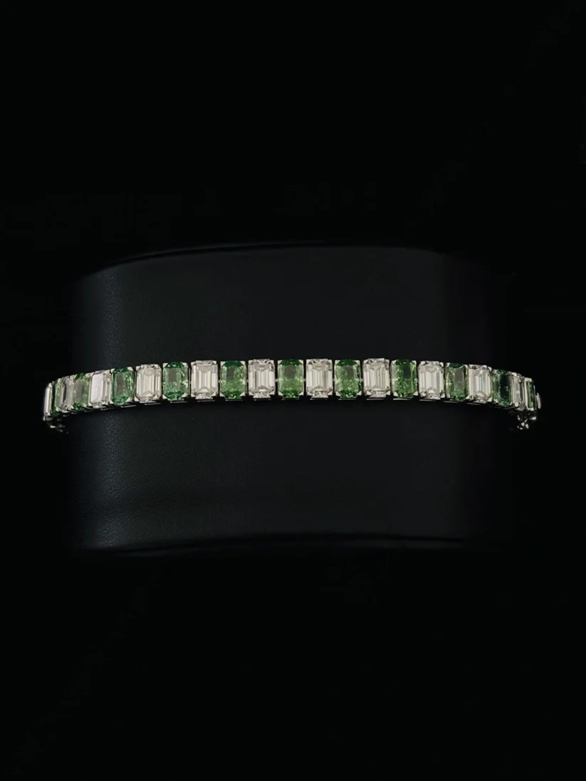 Tennis bracelet features alternating emerald-cut green, and baguette-cut diamond in a silver setting