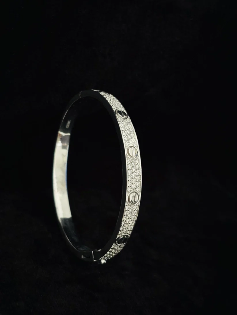 A side view Silver pave diamond luxury screw motif bangle bracelet against a black background