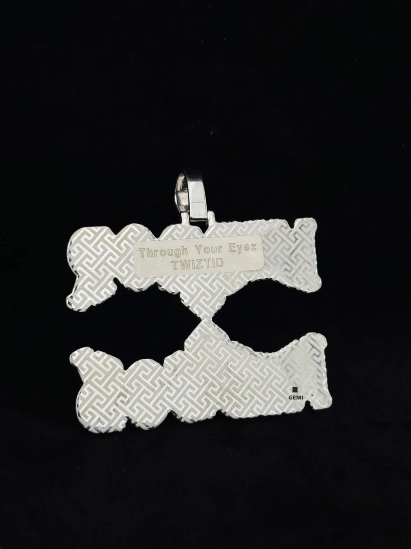 back view Back of a iced-out silver chain pendant featuring a patterned texture and engraved text.