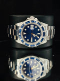 A luxury wristwatch with a silver-tone oyster, a blue dial, and a bezel set with blue stones