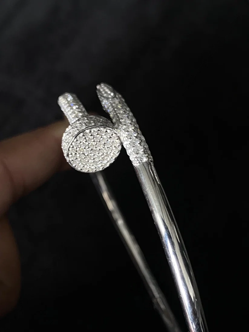 A close-up of a silver bangle bracelet pave-set stone center and matching pave-covered bands, held by a hand 