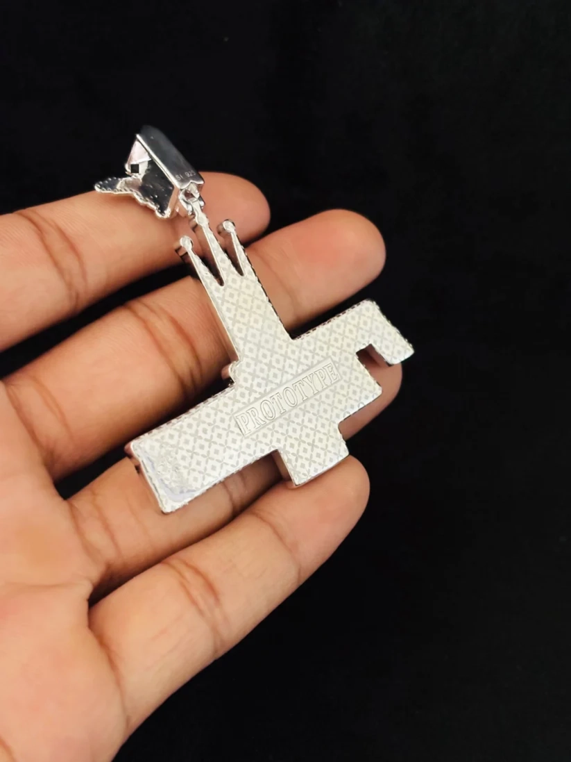 A silver metallic cross pendant with a textured pattern 
