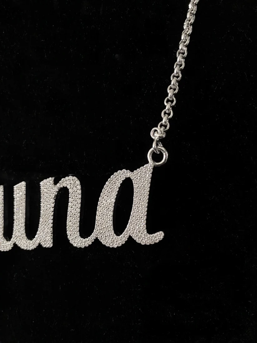 Silver custom cursive name necklace studded with pavé crystals on a delicate silver link chain against a black background.