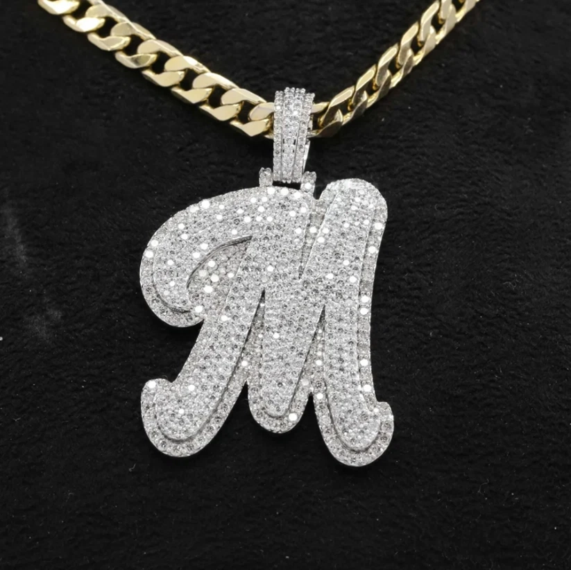 Cursive letter M pendant necklace iced out with pavé diamonds on a gold Cuban link chain.