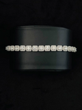 A silver tennis bracelet with a row of square-cut stones, displayed on a black cylindrical jewelry stand