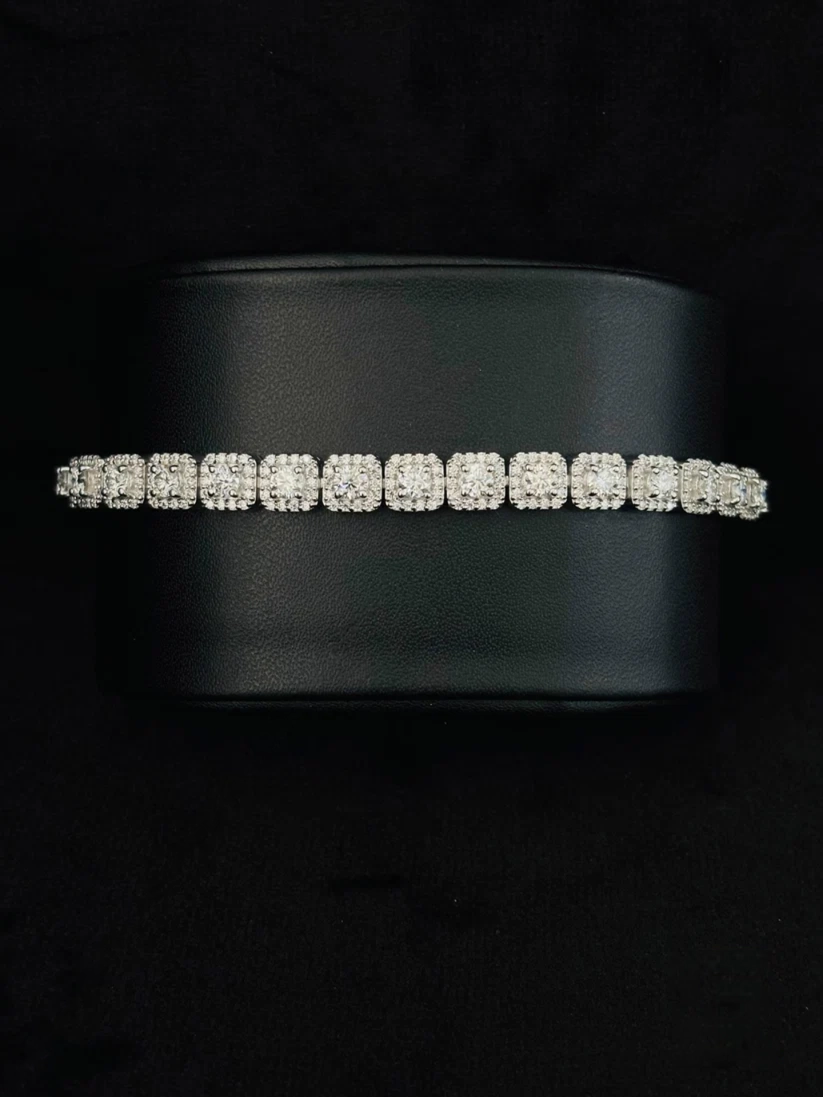 A silver tennis bracelet with a row of square-cut stones, displayed on a black cylindrical jewelry stand