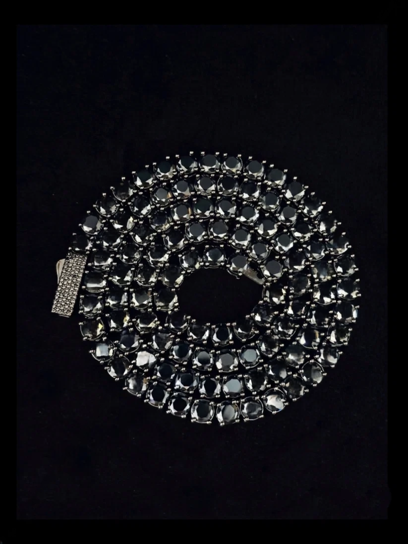 Black diamond tennis chain necklace coiled on a dark background with a pave diamond clasp