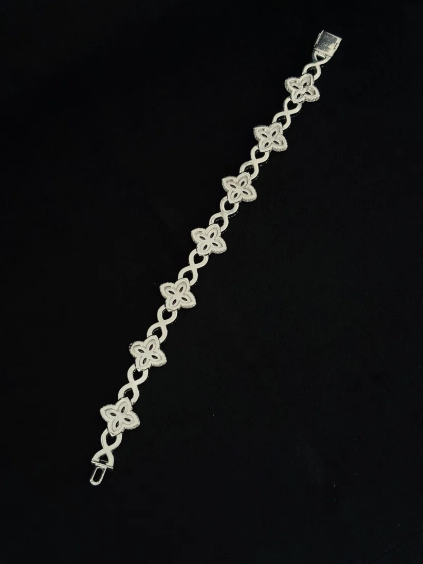 Sterling silver four-leaf clover bracelet with infinity links on a black background