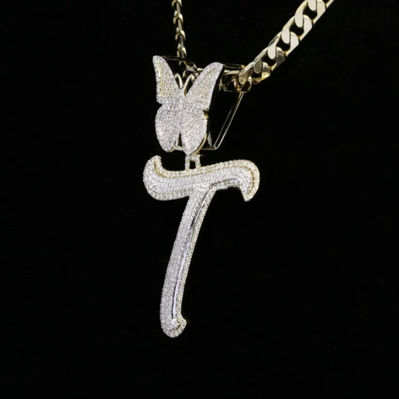 Iced out moissanite diamond cursive initial T pendant with butterfly accent on a gold cuban link chain.